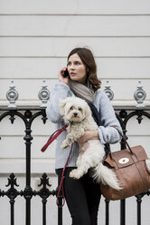 UK, London, junge Frau hält ihren Hund, während sie mit ihrem Smartphone telefoniert - MAUF000177