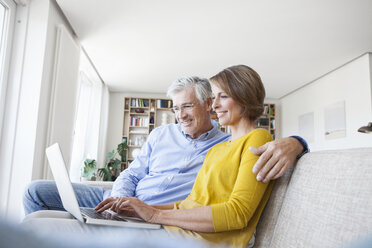Lächelndes Paar sitzt auf der Couch zu Hause und benutzt einen Laptop - RBF003747