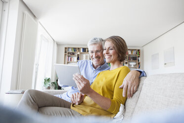 Lächelndes Paar, das zu Hause auf der Couch sitzt und ein digitales Tablet benutzt - RBF003748