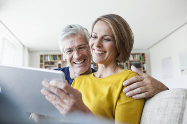 Lächelndes Paar, das zu Hause auf der Couch sitzt und ein digitales Tablet benutzt - RBF003758