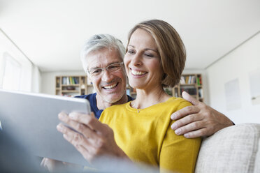 Smiling couple sitting on the couch at home using digital tablet - RBF003758