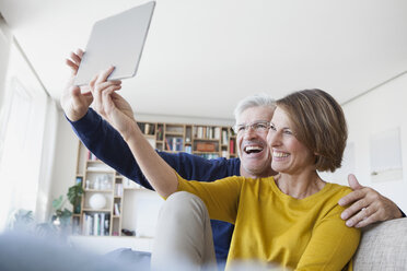 Happy couple sitting on the couch at home taking a selfie with digital tablet - RBF003759