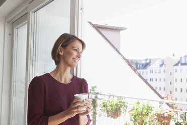 Smiling woman leaning against balcony door looking at distance - RBF003770