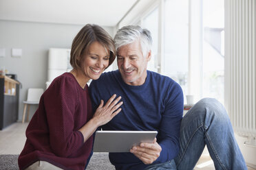 Smiling couple sitting on the floor at home looking at digital tablet - RBF003780