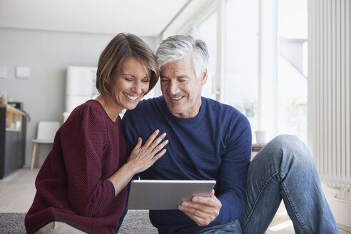 Lächelndes Paar sitzt zu Hause auf dem Boden und schaut auf ein digitales Tablet - RBF003780