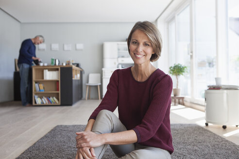 Porträt einer lächelnden Frau, die zu Hause auf dem Boden sitzt - RBF003781