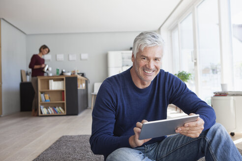Porträt eines lächelnden Mannes, der zu Hause mit einem digitalen Tablet auf dem Boden sitzt - RBF003782
