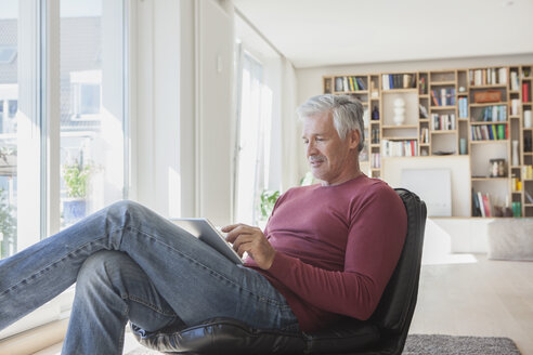 Reifer Mann entspannt sich auf einem Ledersessel zu Hause und benutzt ein digitales Tablet - RBF003797