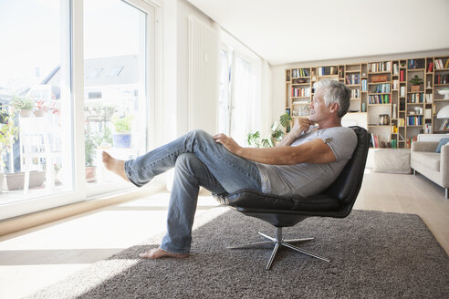 Nachdenklicher Mann entspannt sich auf einem Ledersessel zu Hause und schaut durch das Fenster - RBF003799