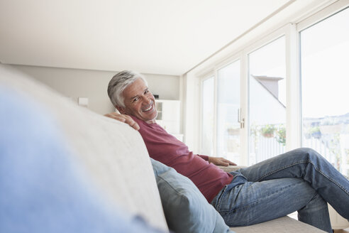 Porträt eines lächelnden Mannes, der zu Hause auf der Couch sitzt - RBF003805