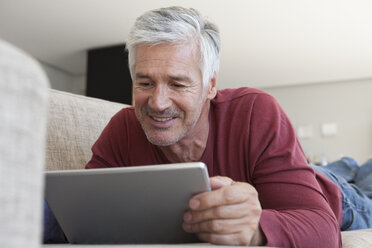 Porträt eines lächelnden Mannes, der zu Hause auf der Couch liegt und ein digitales Tablet benutzt - RBF003811