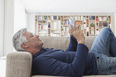 Reifer Mann auf der Couch liegend zu Hause mit digitalem Tablet - RBF003813