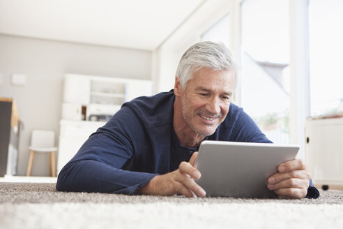 Lächelnder Mann, der zu Hause auf dem Boden liegt und ein digitales Tablet benutzt - RBF003822