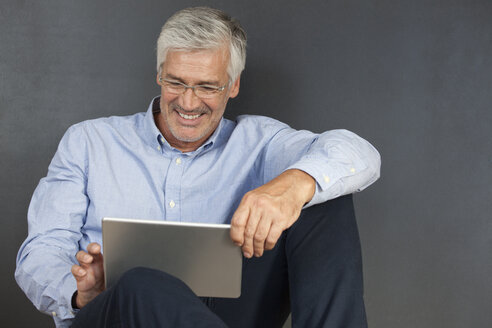 Lächelnder reifer Mann, der auf dem Boden sitzt und ein digitales Tablet benutzt - RBF003830