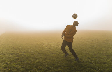 Junger Mann spielt Fußball auf einer Wiese am Abend - UUF006212