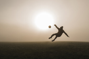 Junger Mann spielt Fußball auf einer Wiese am Abend - UUF006219