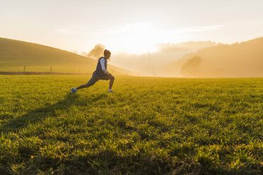 Young man stretching on meadow in the morning - UUF006241