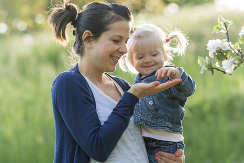 Mutter zeigt ihrer kleinen Tochter die Blüten eines Baumes, lizenzfreies Stockfoto