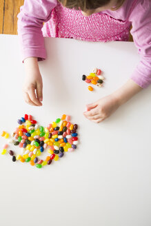 Kleines Mädchen spielt mit Jelly Beans auf einem Tisch - LVF004349
