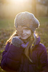 Portrait of smiling girl at evening twilight covering one eye with an autumn leaf - SARF002422