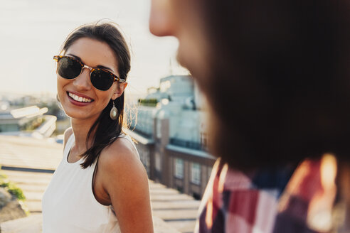 Österreich, Wien, Porträt einer lächelnden jungen Frau mit Sonnenbrille beim Flirten auf einer Dachterrasse - AIF000129