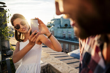 Österreich, Wien, lächelnde junge Frau, die auf einer Dachterrasse ein Foto von ihrem Freund macht - AIF000130