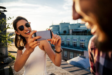 Austria, Vienna, portrait of smiling young woman taking a photo of her boyfriend on a roof terrace - AIF000131