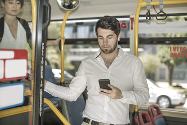 Young man in city bus listening to music from smartphone - ZEF007758