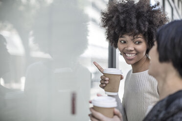 Zwei junge Frauen mit Kaffee schauen durch ein Schaufenster - ZEF007769