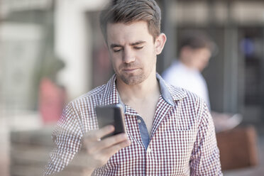 Young man in street looking at smart phone - ZEF007788