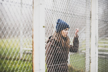 Young woman standing behind mesh wire fence - UUF006251