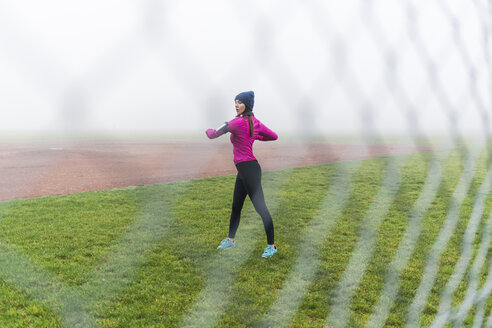 Junge Frau beim Workout auf einer Wiese hinter Maschendrahtzaun - UUF006256