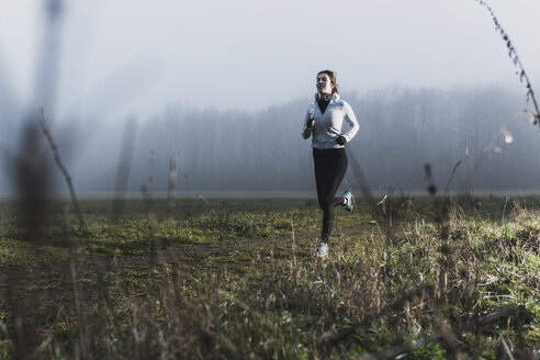 Junge Frau beim Joggen in der Natur an einem diesigen Tag - UUF006269