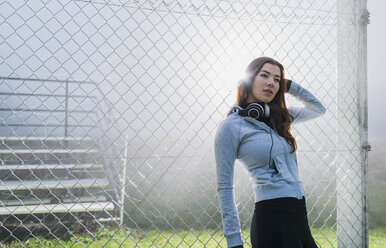 Portrait of young woman wearing sports wear leaning against mesh wire fence - UUF006270