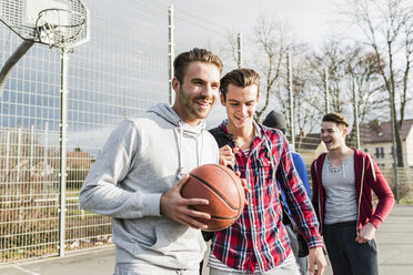 Junger Mann mit Basketball und Freunden auf dem Basketballplatz - UUF006279