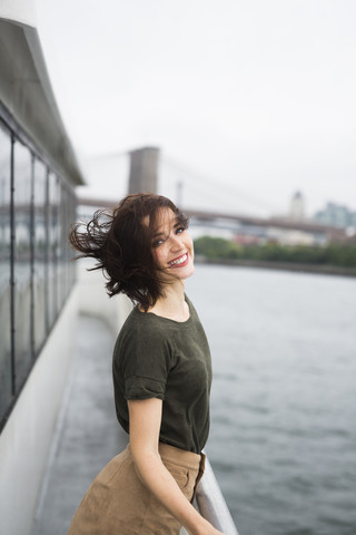 USA, New York City, Porträt einer jungen Frau, die an einem windigen Tag auf einem Ausflugsboot steht, lizenzfreies Stockfoto