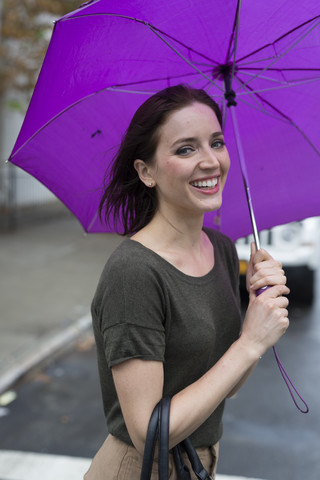 USA, New York City, portrait of smiling young woman standing with umbrella on a rainy day stock photo