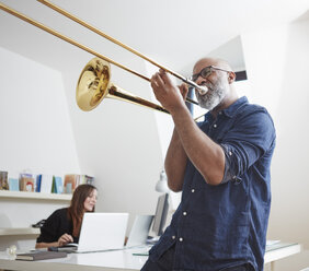 Man playing trombone at home office - RHF001148