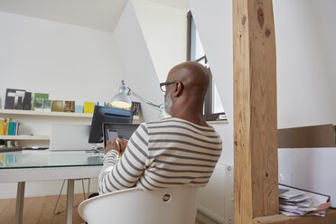 Rückenansicht eines Mannes, der an seinem Schreibtisch im Büro sitzt und sein Smartphone benutzt - RHF001156