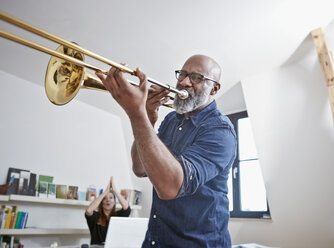 Portrait of man playing trombone at home office - RHF001158