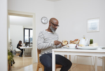 Man having late breakfast at his home office - RHF001165