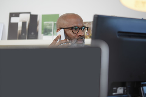 Porträt eines Mannes, der hinter einem Computerbildschirm sitzt und telefoniert, lizenzfreies Stockfoto