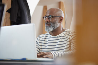 Porträt eines Mannes, der mit seinem Laptop am Schreibtisch seines Büros sitzt - RHF001181