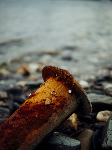 Rostiges Rohr und Kieselsteine am Flussufer, lizenzfreies Stockfoto