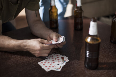 Junger Mann hält Spielkarten auf einem Tisch mit Bierflaschen - ZEF007828