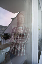 Porträt einer jungen Frau mit einer Tasse Kaffee, die durch ein Fenster schaut - RBF003835