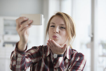 Young woman blowing a kiss while taking a selfie with her smartphone - RBF003841