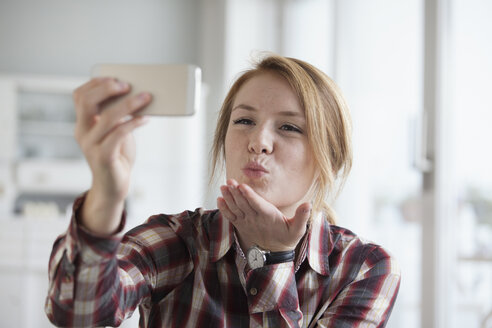 Junge Frau, die sich einen Kuss zuwirft, während sie ein Selfie mit ihrem Smartphone macht - RBF003841