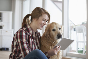 Lächelnde junge Frau sitzt neben ihrem Hund und schaut auf ein digitales Tablet - RBF003845