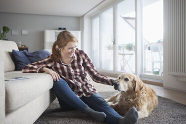 Smiling young woman sitting beside her dog on the floor at home - RBF003849